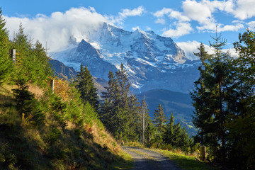 The gravel mountain road and Jungfrau peak view in the clouds near Swiss Alpine village Wengen in Switzerland.