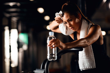 Exhausted athletic woman having a water break while working out on exercise bike.