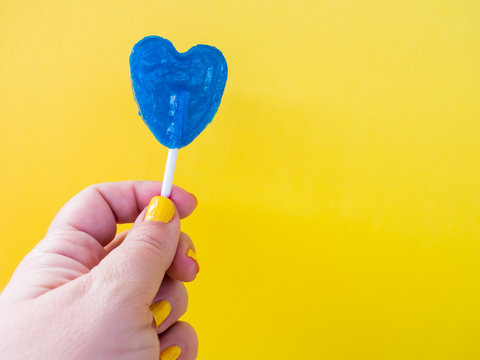 A woman with yellow painted nails with a blue lollipop in her hand and yellow background