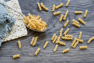 flat lay silver spoon  spiralli pasta on wooden background.