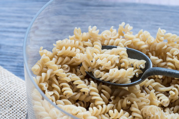 flat lay silver spoon with heap pasta spiralli, on tablecloth and wooden background
