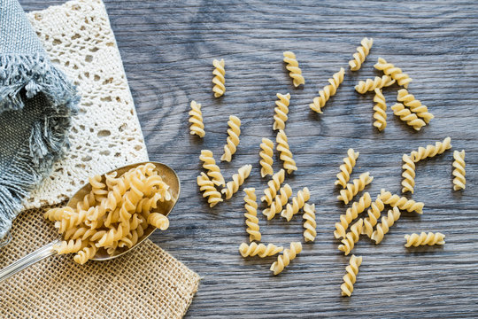 flat lay silver spoon  spiralli pasta on wooden background.