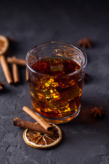 Glass of brandy or whiskey, spices and decorations on dark background. Seasonal holidays concept.