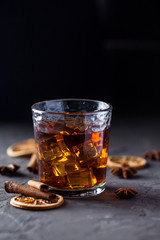 Glass of brandy or whiskey, spices and decorations on dark background. Seasonal holidays concept.