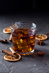 Glass of brandy or whiskey, spices and decorations on dark background. Seasonal holidays concept.