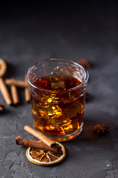 Glass of brandy or whiskey, spices and decorations on dark background. Seasonal holidays concept.