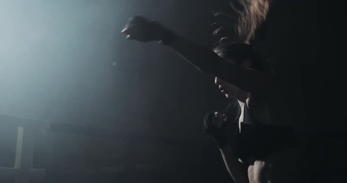 Female boxer training in the dark ring. Slow motion. Silhouette. Boxing concept
