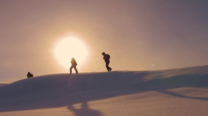 Fototapeta na wymiar team of climbers follow each other along snow ridge in rays of yellow sunt. work in team of tourists, overcoming difficulties to move to victory and success. silhouettes of travelers go to victory