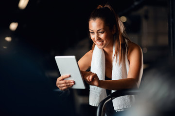 Young athletic woman using digital tablet while working out in a gym.