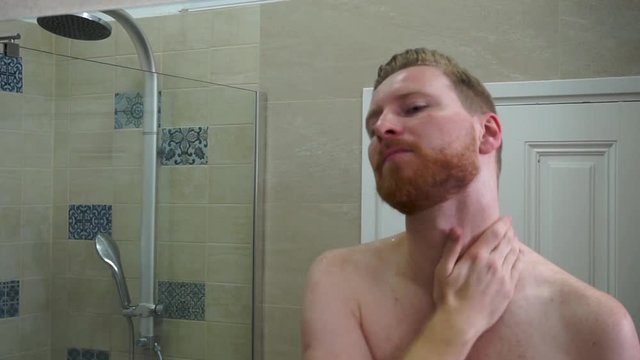 Young caucasian man applying face care face cream on his face and neck