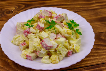 Salad with crab sticks, sweet corn, chinese cabbage, eggs and mayonnaise on wooden table
