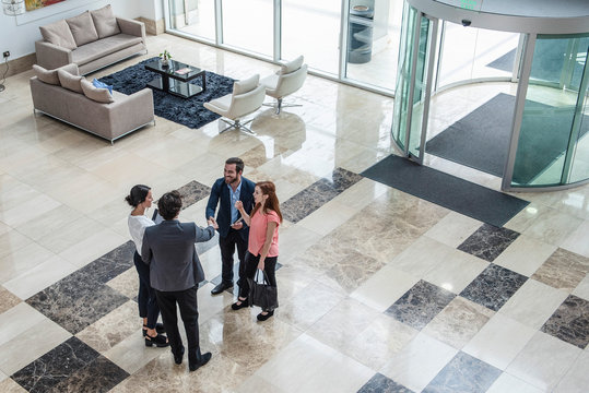 Elevated view of smiling business people greeting each other while standing in hotel lobby