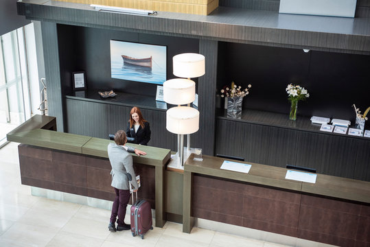 Female receptionist talking with businessman while standing at hotel reception desk