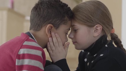 Portrait of cute adorable african american boy and pretty blond caucasian girl touching foreheads each other. Girl hold boys face in hands