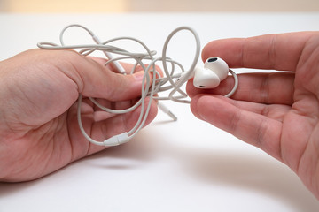 male hands are holding white headphones with tangled wires