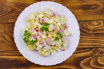 Salad with crab sticks, sweet corn, chinese cabbage, eggs and mayonnaise on wooden table