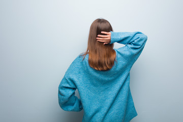 Young pretty woman wearing a blue sweater from behind thinking about something