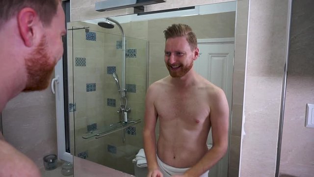 Young caucasian man washing his face in the bathroom wearing white towel