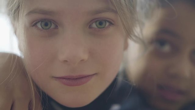 Close-up face of a cute beautiful caucasian girl who is embraced by an adorable African American boy. Pretty smile of adorable blonde girl with green eyes and thin lips.