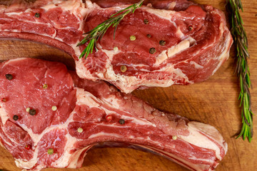Raw fresh beef rib eye steaks on bone with spices and rosemary on wooden table. Top view