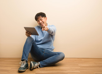 Young chinese man sitting using his tablet cheerful and smiling pointing to front