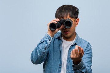 Young chinese man holding a binoculars inviting to come