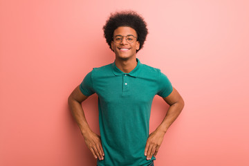 Young african american man over a pink wall with hands on hips