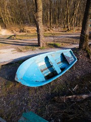 small old shabby worn wooden rescue boat, painted blue, early spring landscape with bare trees on...