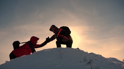 team work and victory. Tourists extends hand to friend that rises to top of hill. Climbers in...
