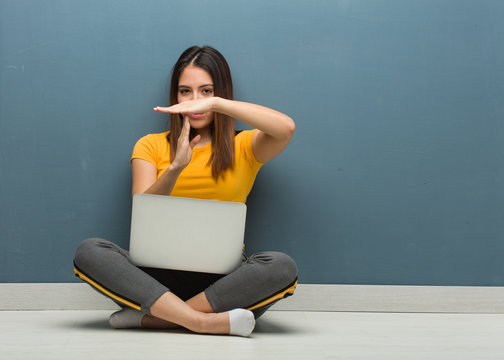 Young woman sitting on the floor with a laptop doing a timeout gesture