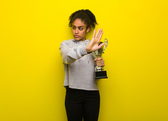 Young fitness black woman putting hand in front. Holding a trophy.