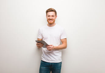 Young redhead man cheerful with a big smile. Holding a tablet. - obrazy, fototapety, plakaty