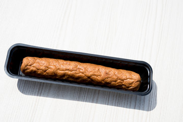 close up Dutch fried snack frikandel in black plastic bowl, on white table