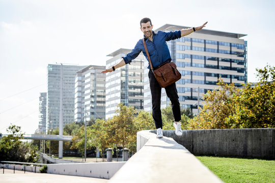 Smiling man with leather bag balancing on wall