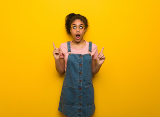 Young black african american girl with blue eyes surprised pointing up to show something