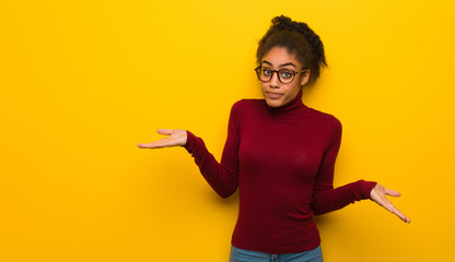 Young black african american girl with blue eyes doubting and shrugging shoulders