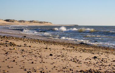 Fototapeta na wymiar Sea coast with beach full of pebbles. Seashore with surf waves. Empty sand beach. Dramatic coastline. Wide beach. Summer vacation concept. Vast landscape.
