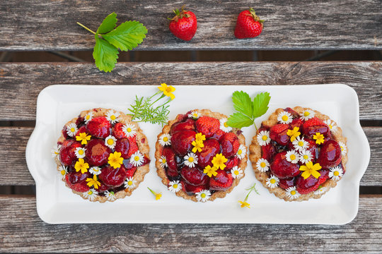 Homemade strawberry heart tartlets with daisy flowers and golden marigold, edible flowers, dark wood
