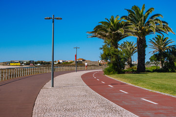 Esposende, Portugal - 10/03/2018: Empty road to beach with palms. Health path along seacoast. Travel and vacation concept. Empty street with palm trees. Sunny day in Portugal. Walkway near the ocean.