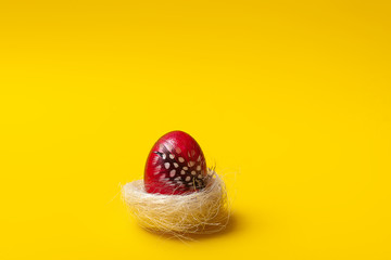 Easter, pink egg on yellow background. Decorated with feathers. 