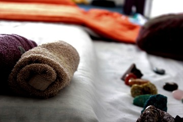 Close up view of mattress with white and orange sheets, stones, crystals and towels wrapped in...