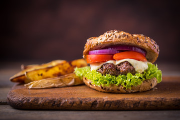 Home made hamburger with green salad and with american potatoes behind. Brown wooden background.