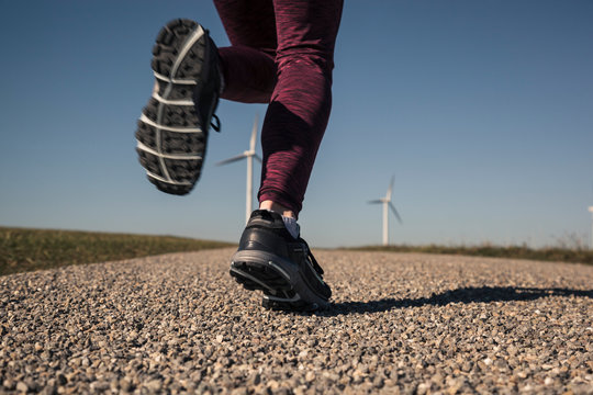Young woman jogging on field way, wind wheels in the background