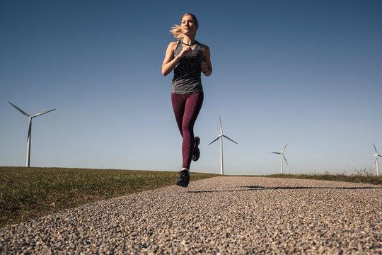 Young woman jogging on field way, wind wheels in the background - Powered by Adobe