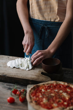 Young man preparing pizza, cutting mozzarella on chopping board