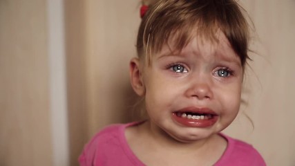 Front view of sad little girl crying, screaming and sobbing at home. Displeased child looking at camera with wet eyes and weeping. Small kid with tears on face. Concept of unhappiness and childhood.