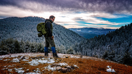 A Hiker Man with Backpack Standing on a Snowy Slope 