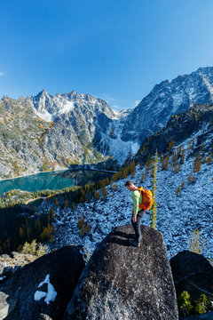 A man with a pack scrambles up a rocky ridge amidst fall colors near Colchuck Lake in the Cascade Range of Washington State.