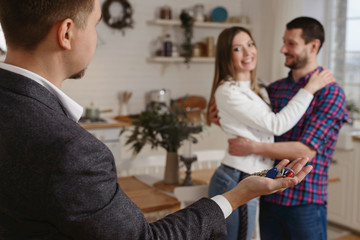 Male estate agent showing and giving new home keys to a young happy caucasian couple in their new flat or house