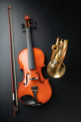A new shining violin and an old trumpet on a dark table. Musical instruments, stringed and wind.